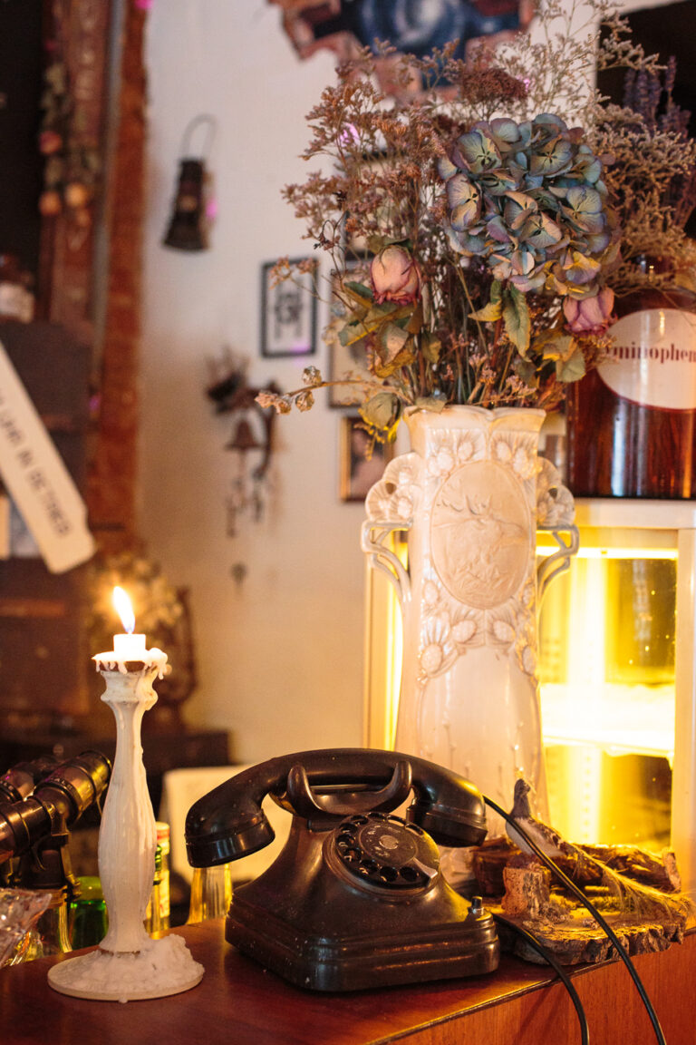 antiker schwarzes Telefon daneben eine weisse Blumenvase mit Trockenpflanzen Kerzenständer