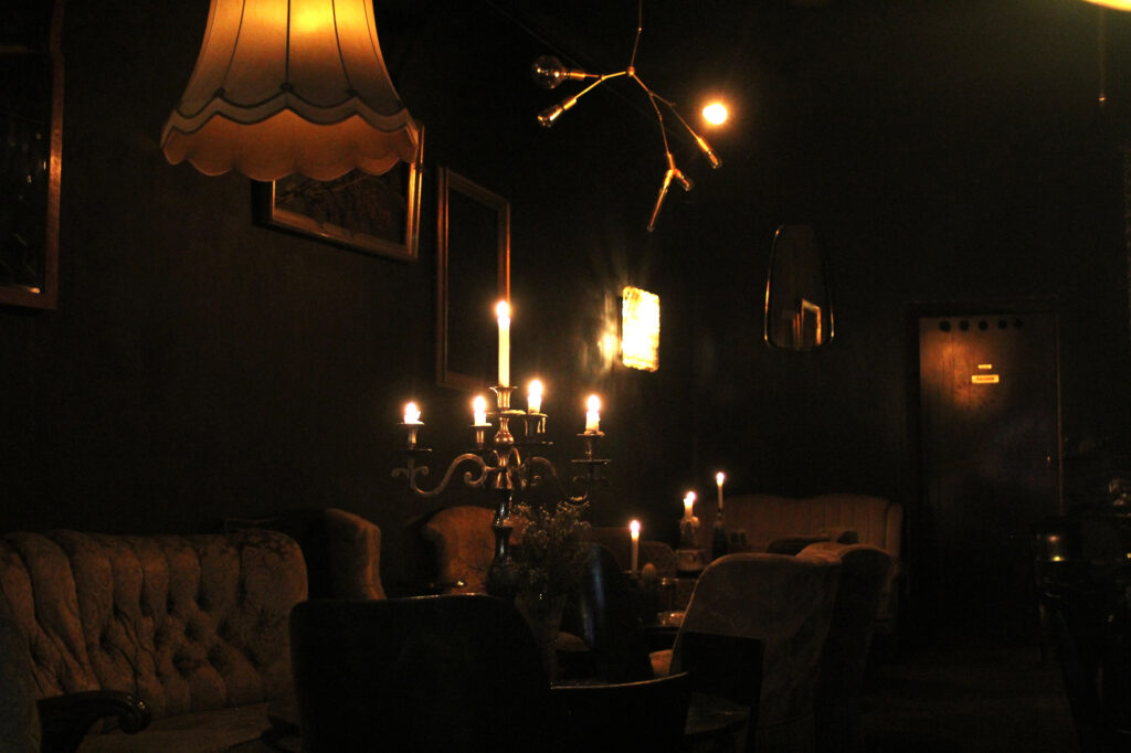 dunkler Raum mit unterschiedlichen Sitzmöbeln und Beleuchtungen